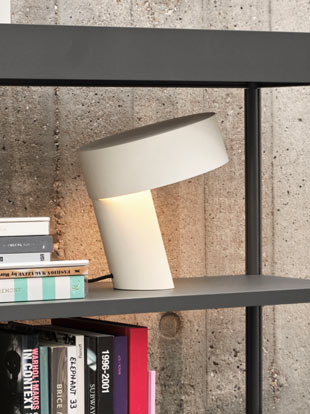 A white Slant lamp by HAY, positioned on a black bookcase in a home setting.